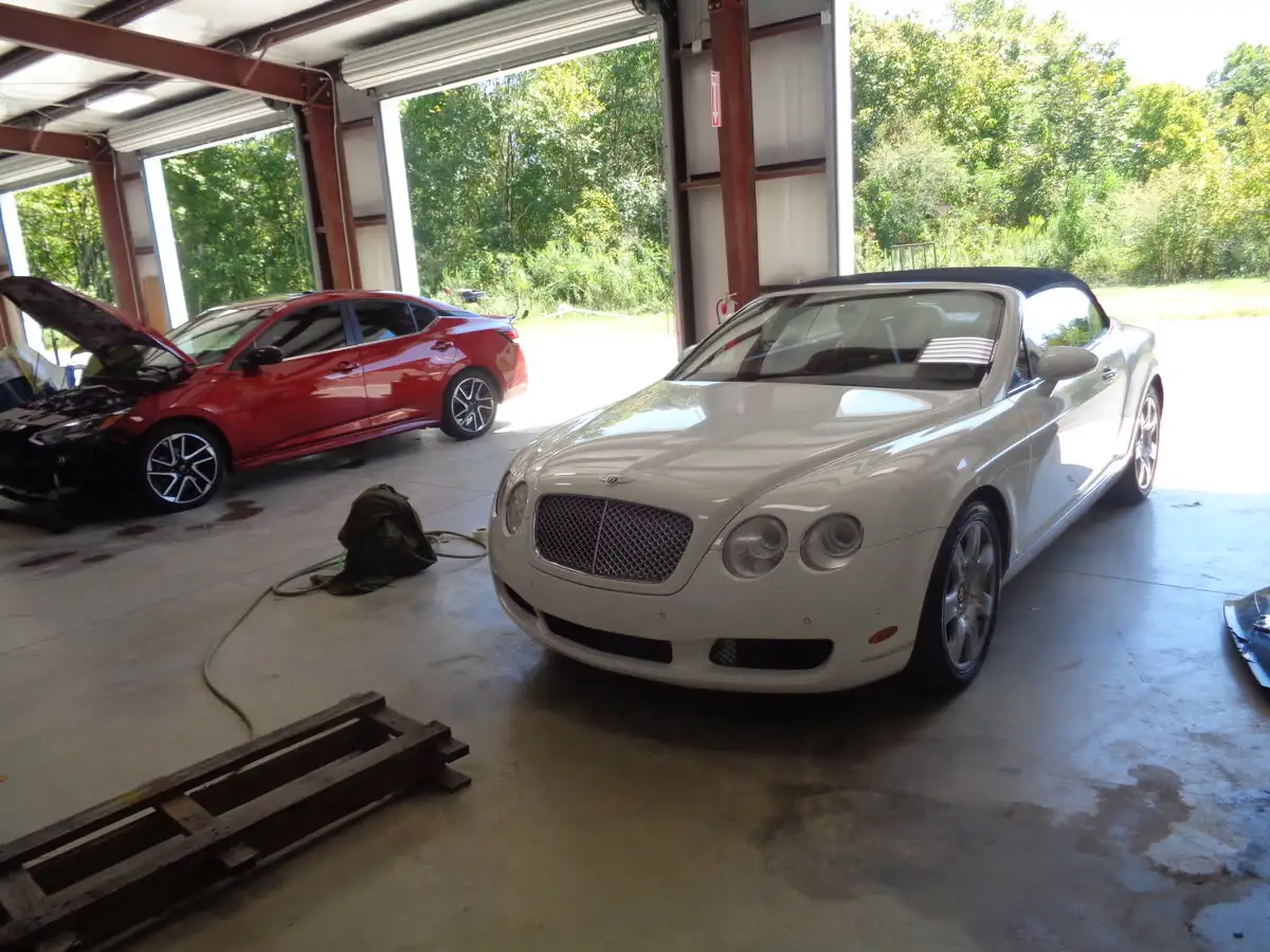 White convertible and red sedan with its hood open inside a repair bay at Ron's Body & Paint Shop
