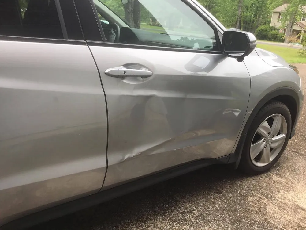 Silver SUV with a deep dent and crease across its front passenger door before repair